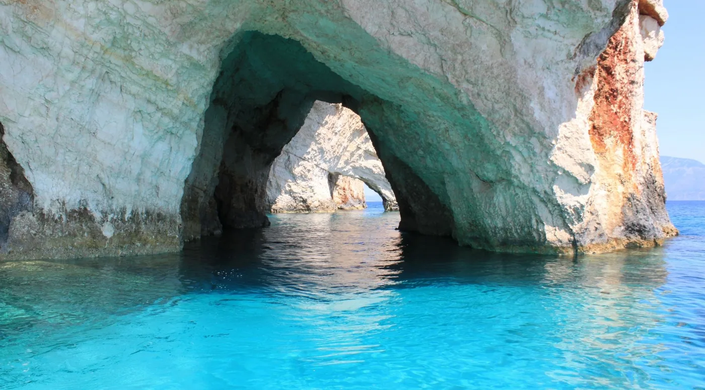 A tall sea arch at the Blue Caves with white limestone reflected in still electric-blue water