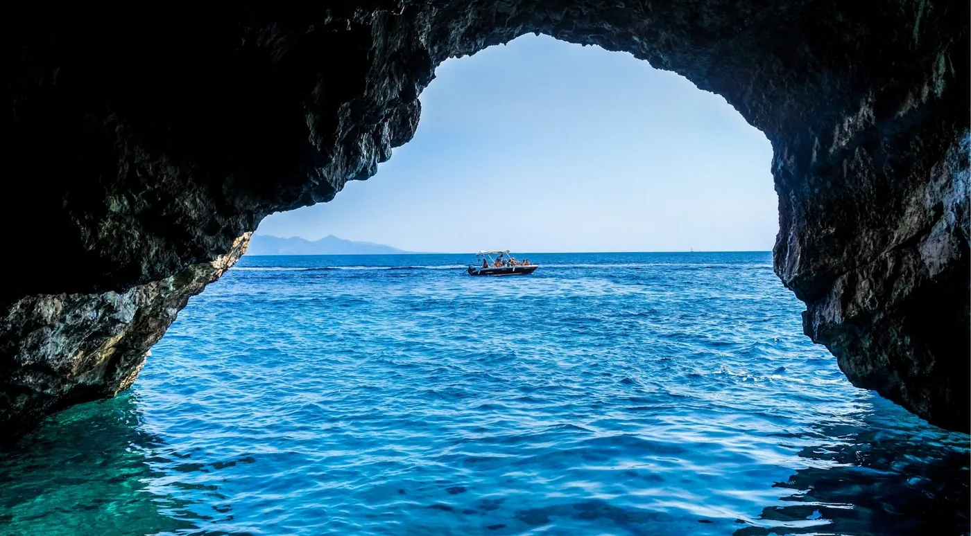 View from inside a dark sea cave out to a small boat on blue water