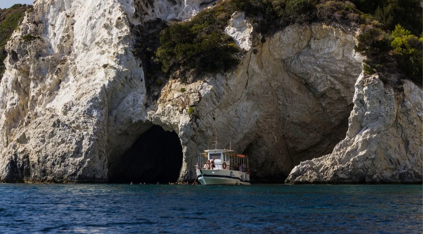 A wooden taxi boat inside a sea cave beneath a pale limestone arch