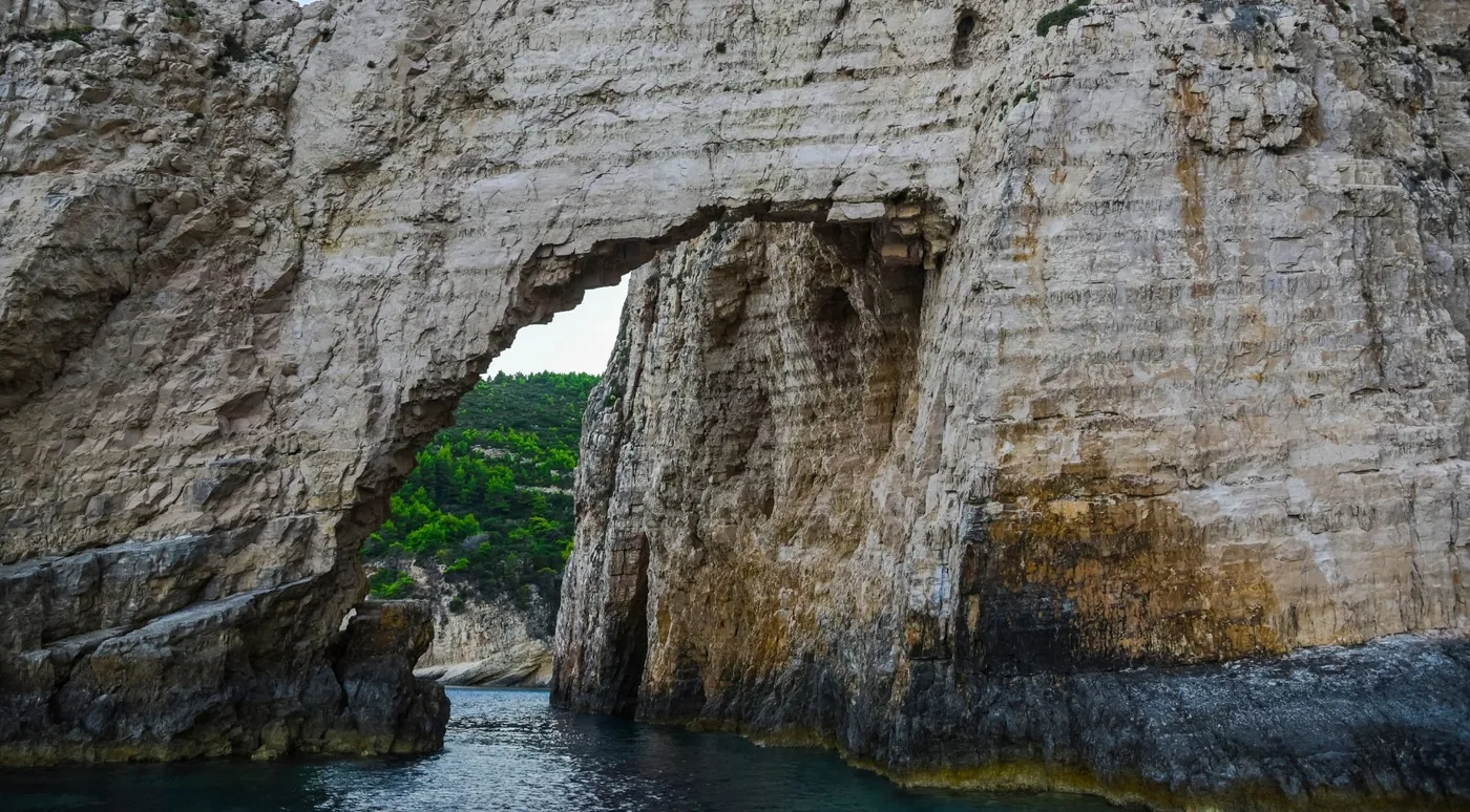 A limestone arch with greenery on top, seen from the water at the Blue Caves