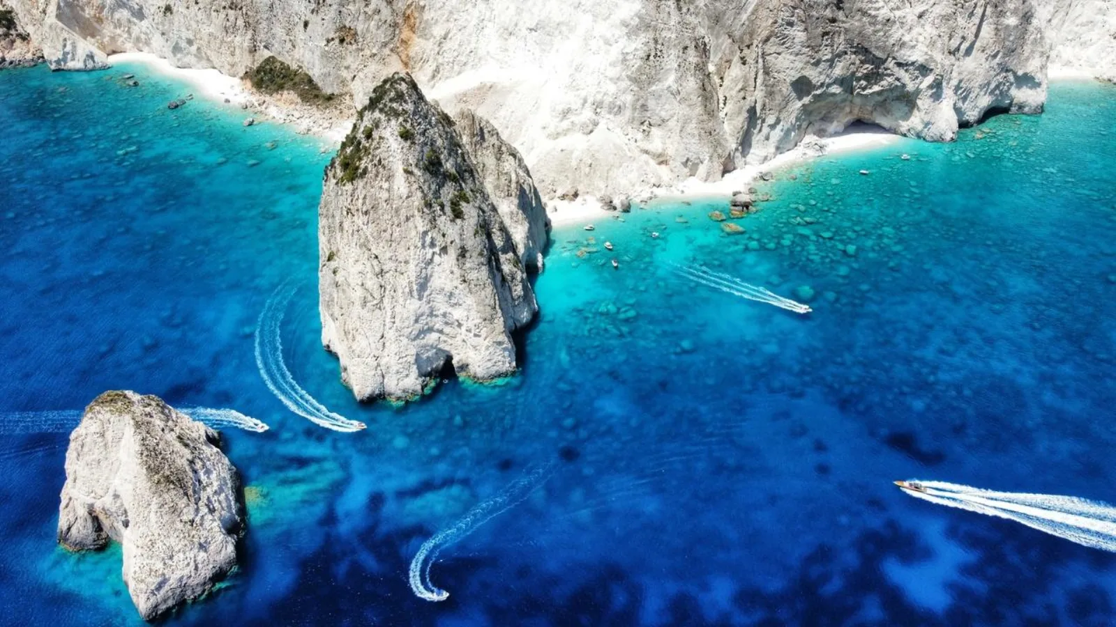 Aerial view of the Mizithres sea stacks with speedboats and a white pebble beach