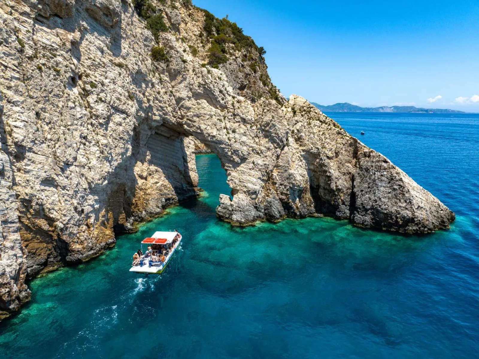 A tour boat passing beneath a natural rock arch on the Keri coast