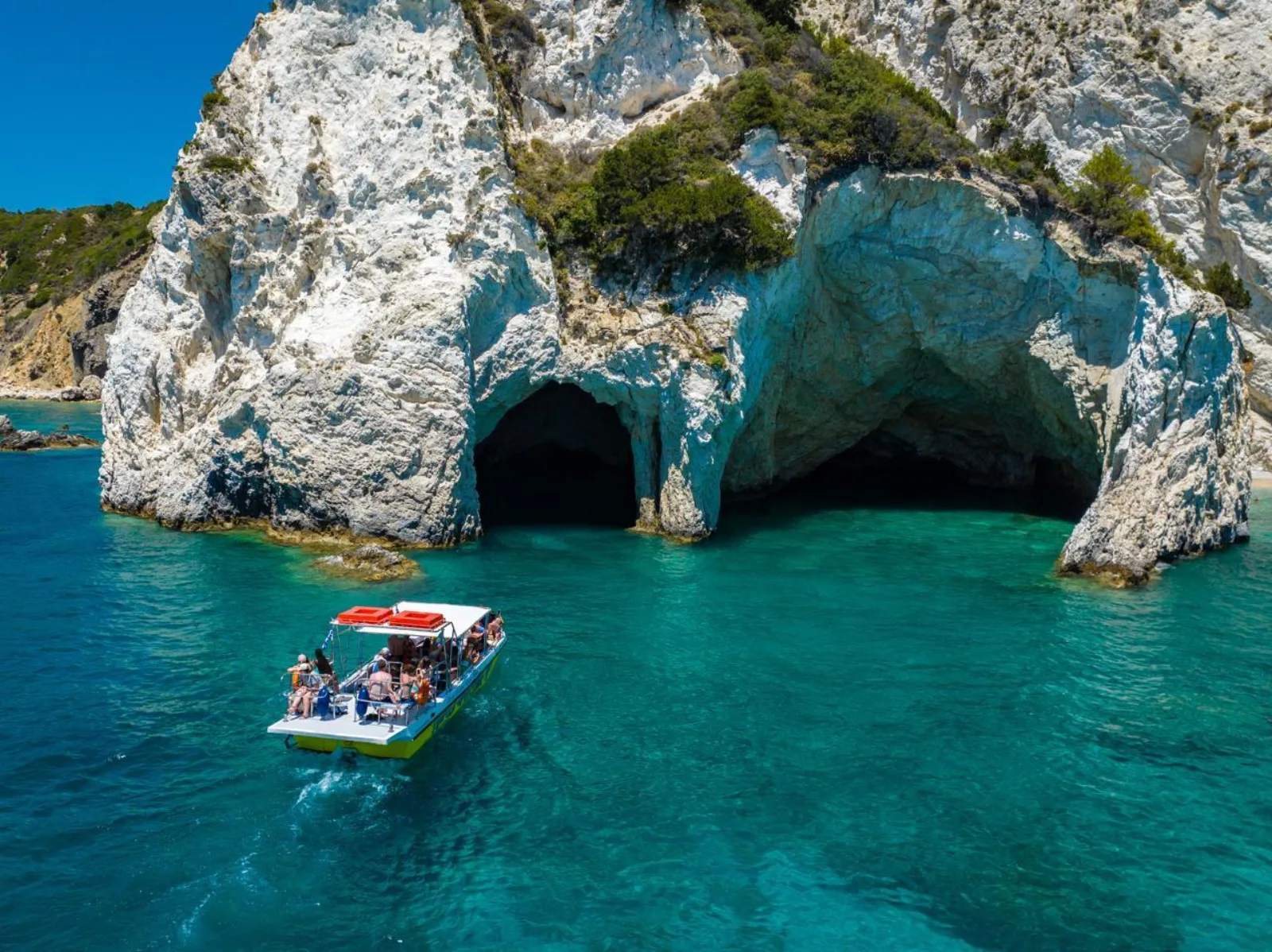 A tour boat at the mouth of a large sea cave under the Keri cliffs