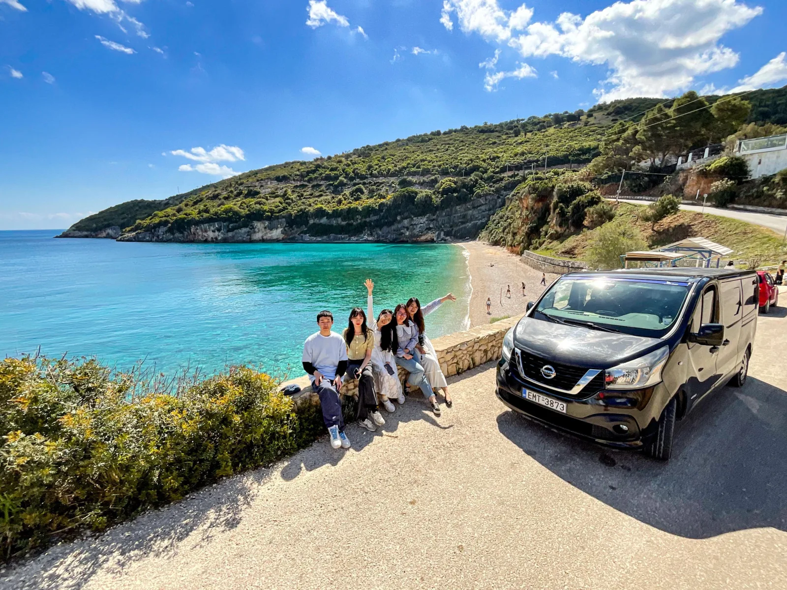 A tour group beside the air-conditioned minibus at a roadside viewpoint over a cove on the north-east coast