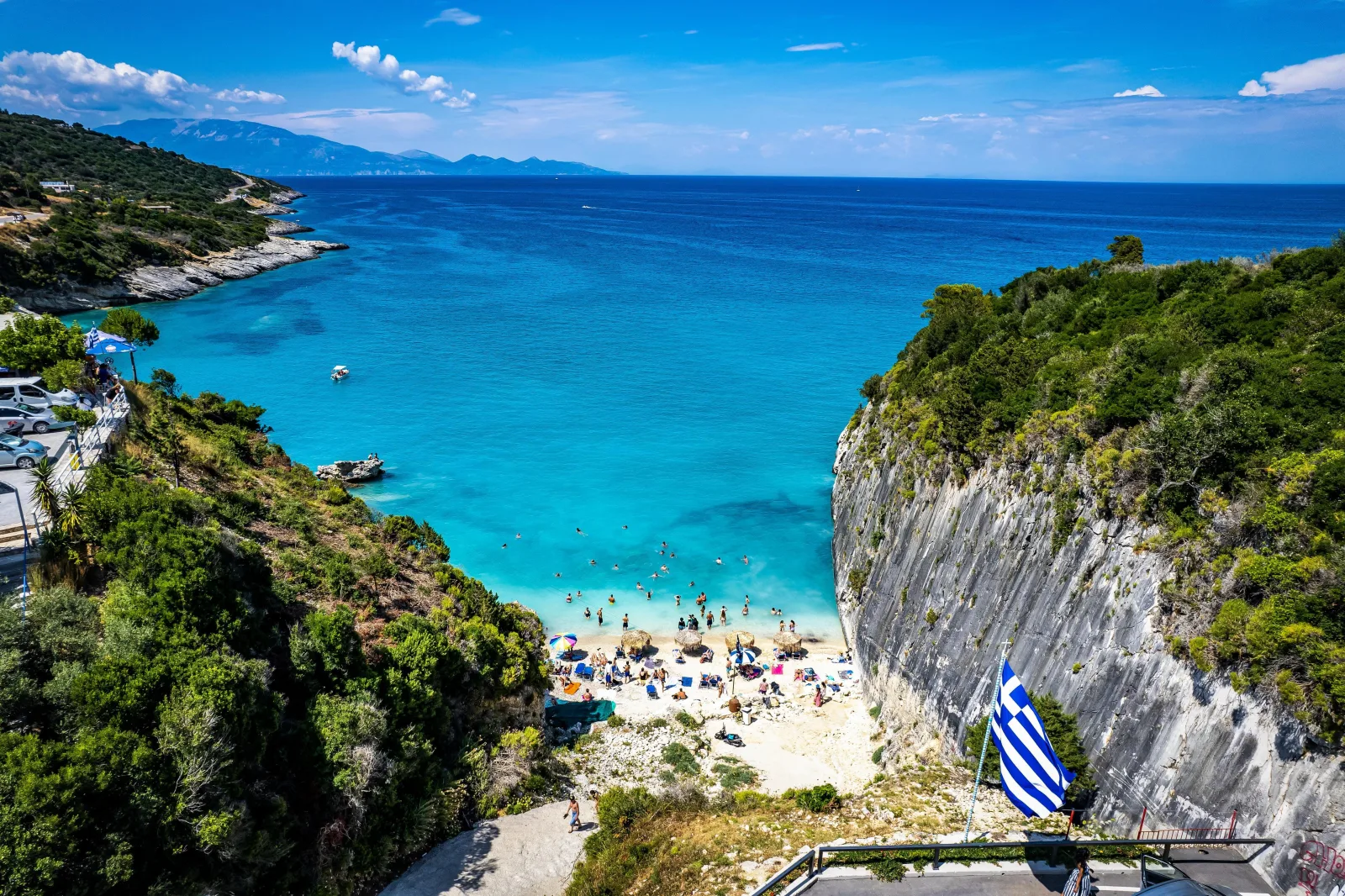 Looking down onto a small cove with sunbeds and a Greek flag on the cliff edge