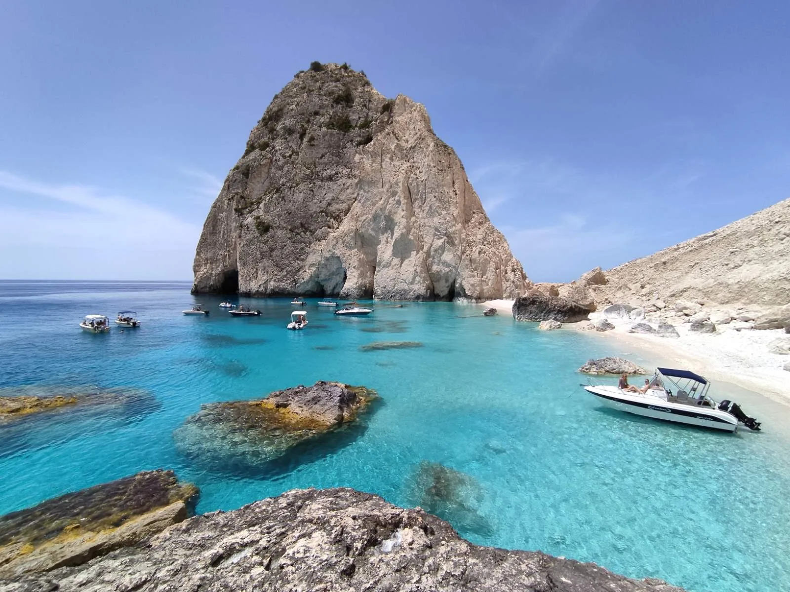 The Mizithres stack from a cove, with boats anchored in the turquoise shallows
