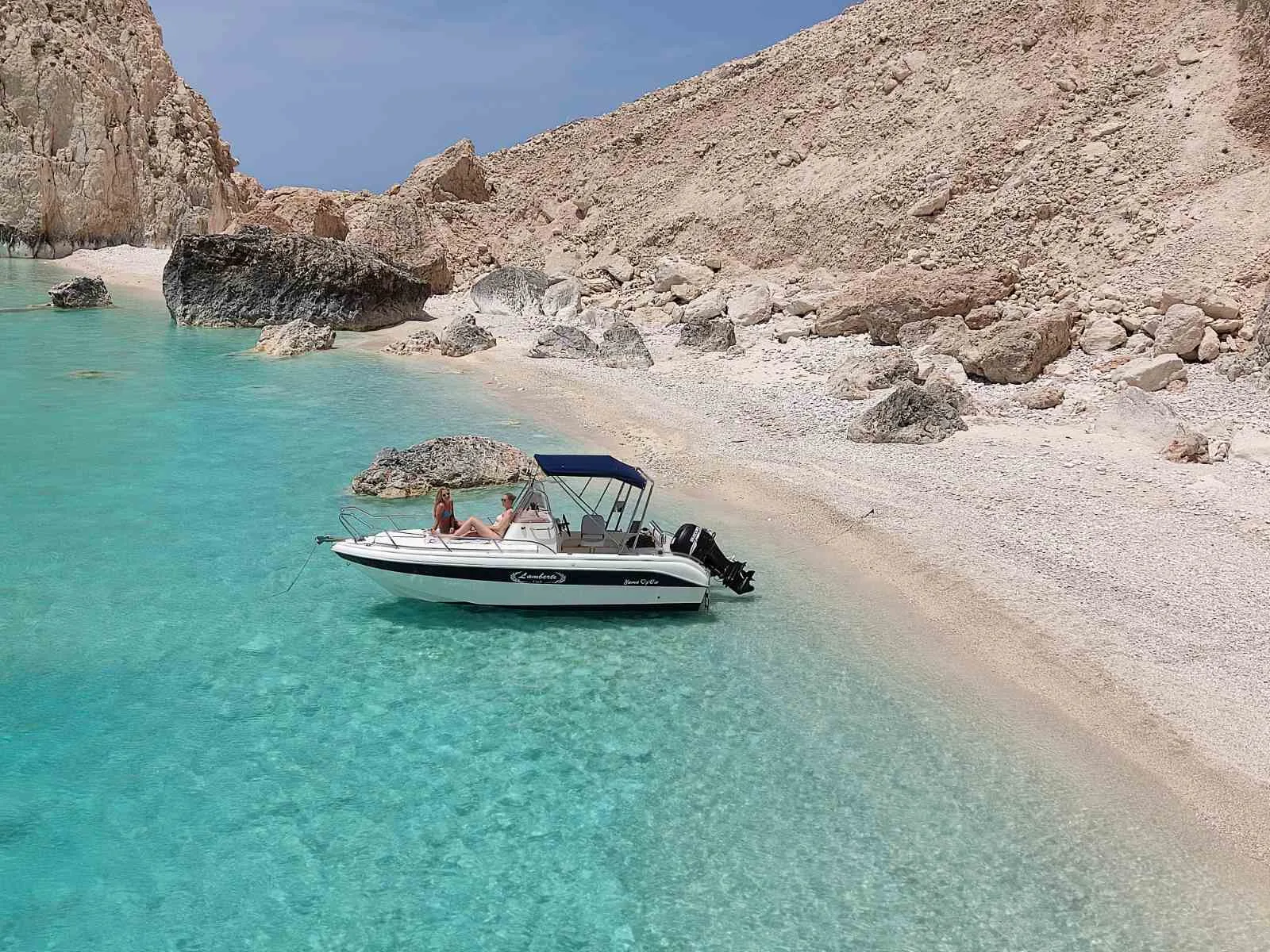 The boat beside a white pebble beach in a hidden cove