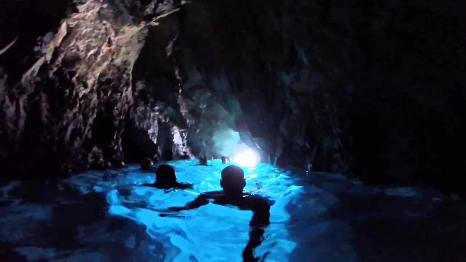 Swimmers inside a dark cave lit by blue light from its entrance