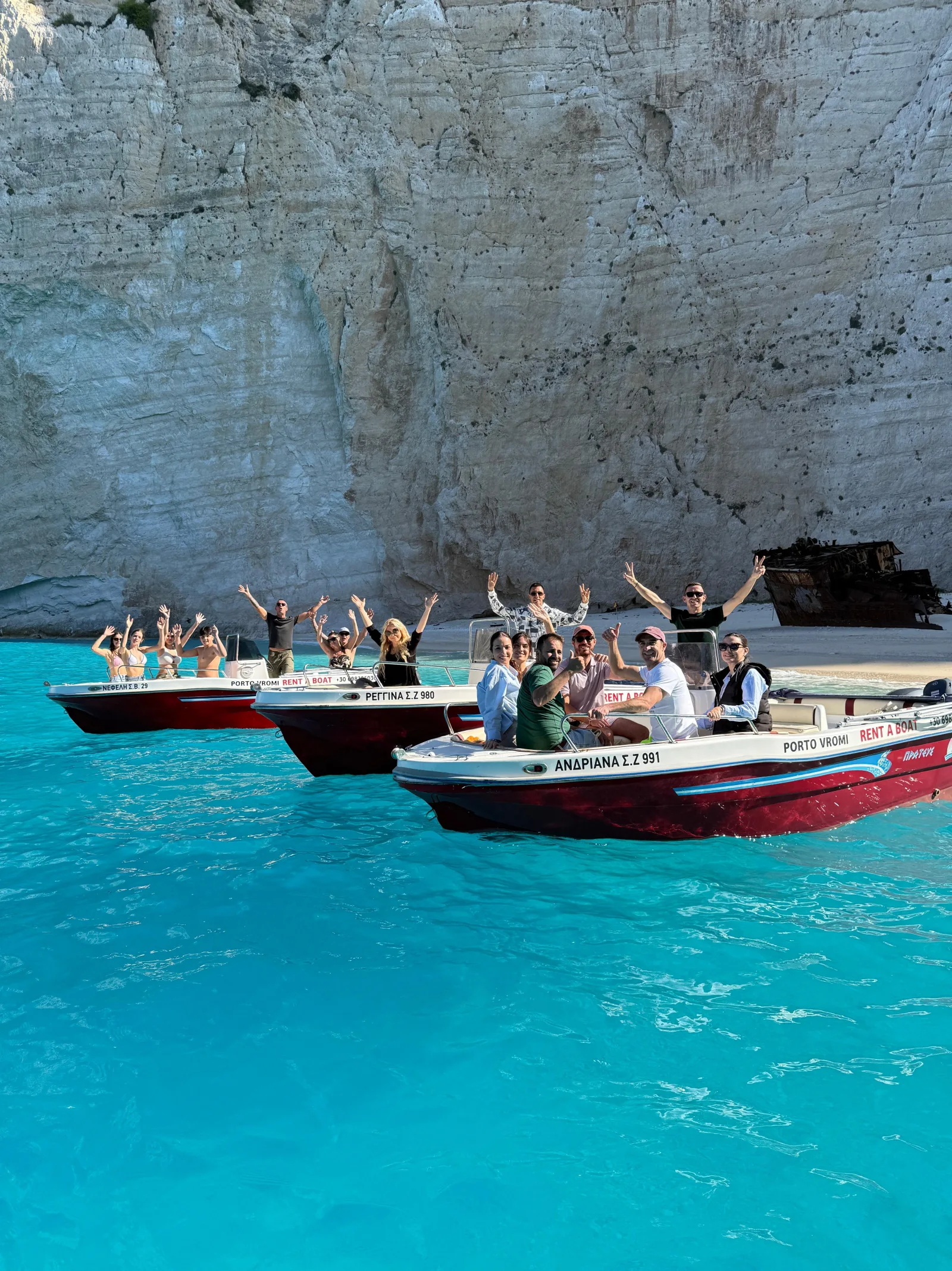 Rental speedboats with waving passengers beneath the Navagio cliffs