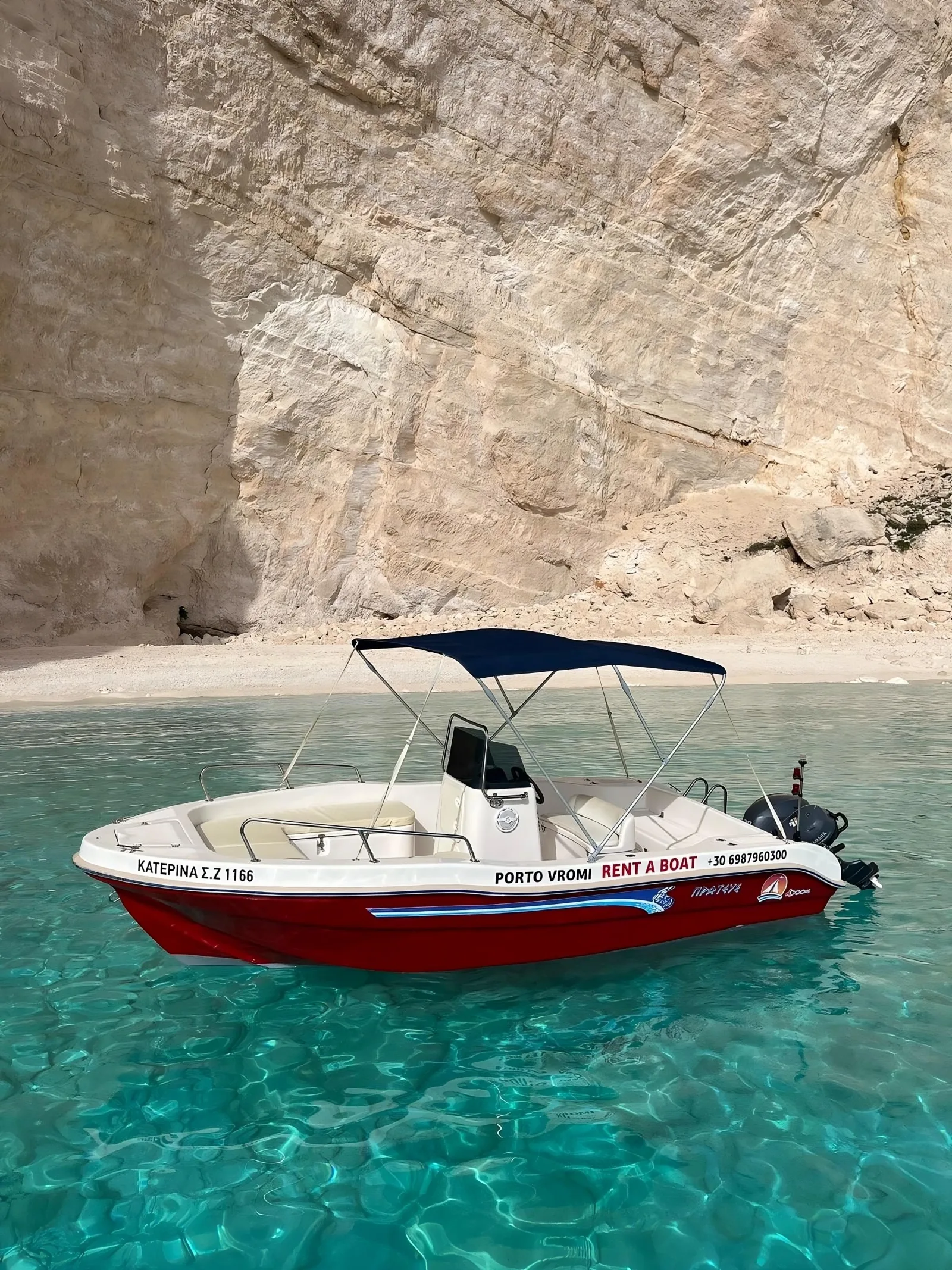 A red-and-white rental boat with a sun canopy moored at a pebble beach under the cliffs