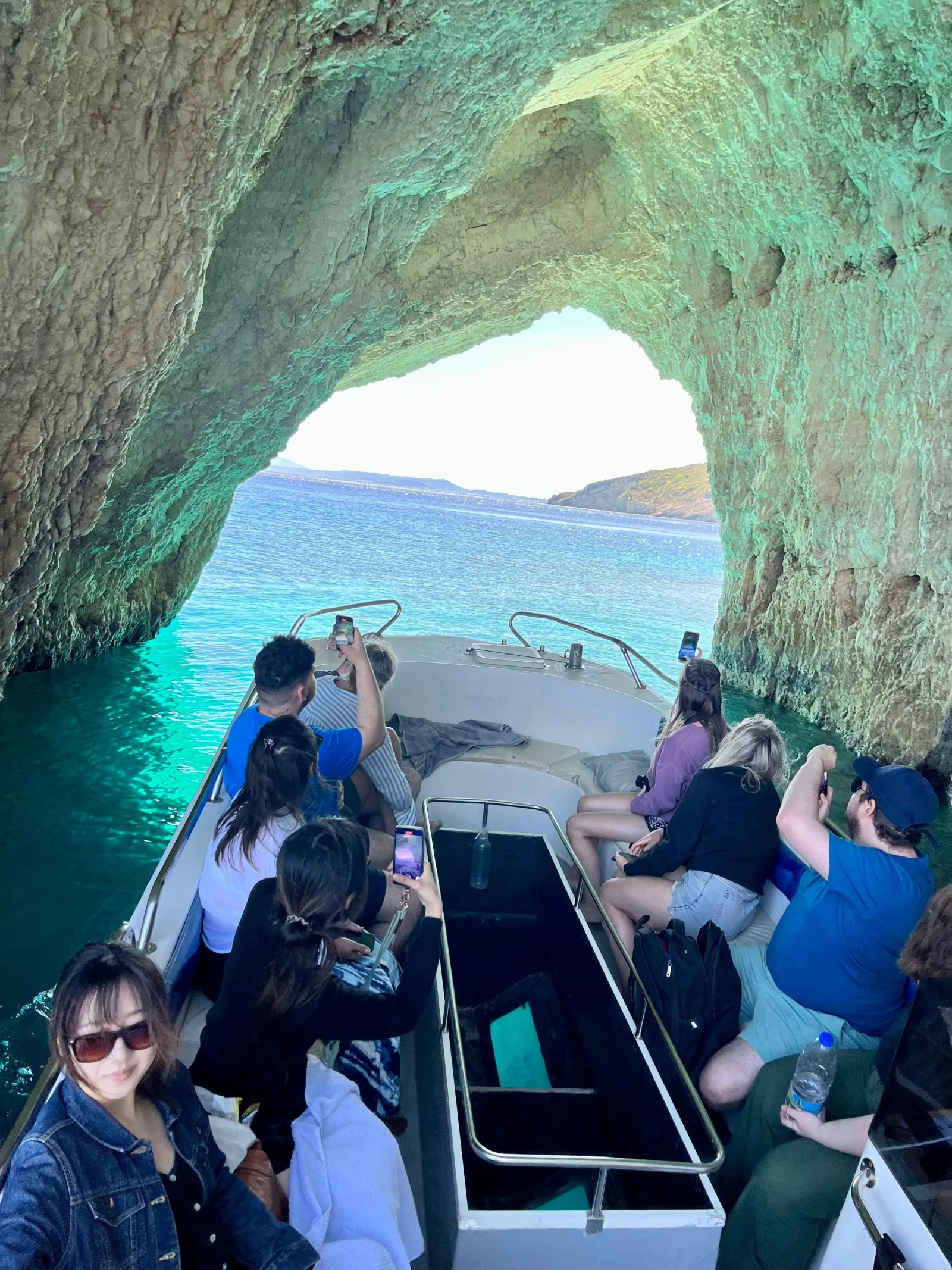 Passengers on a small boat entering a limestone sea arch of the Blue Caves