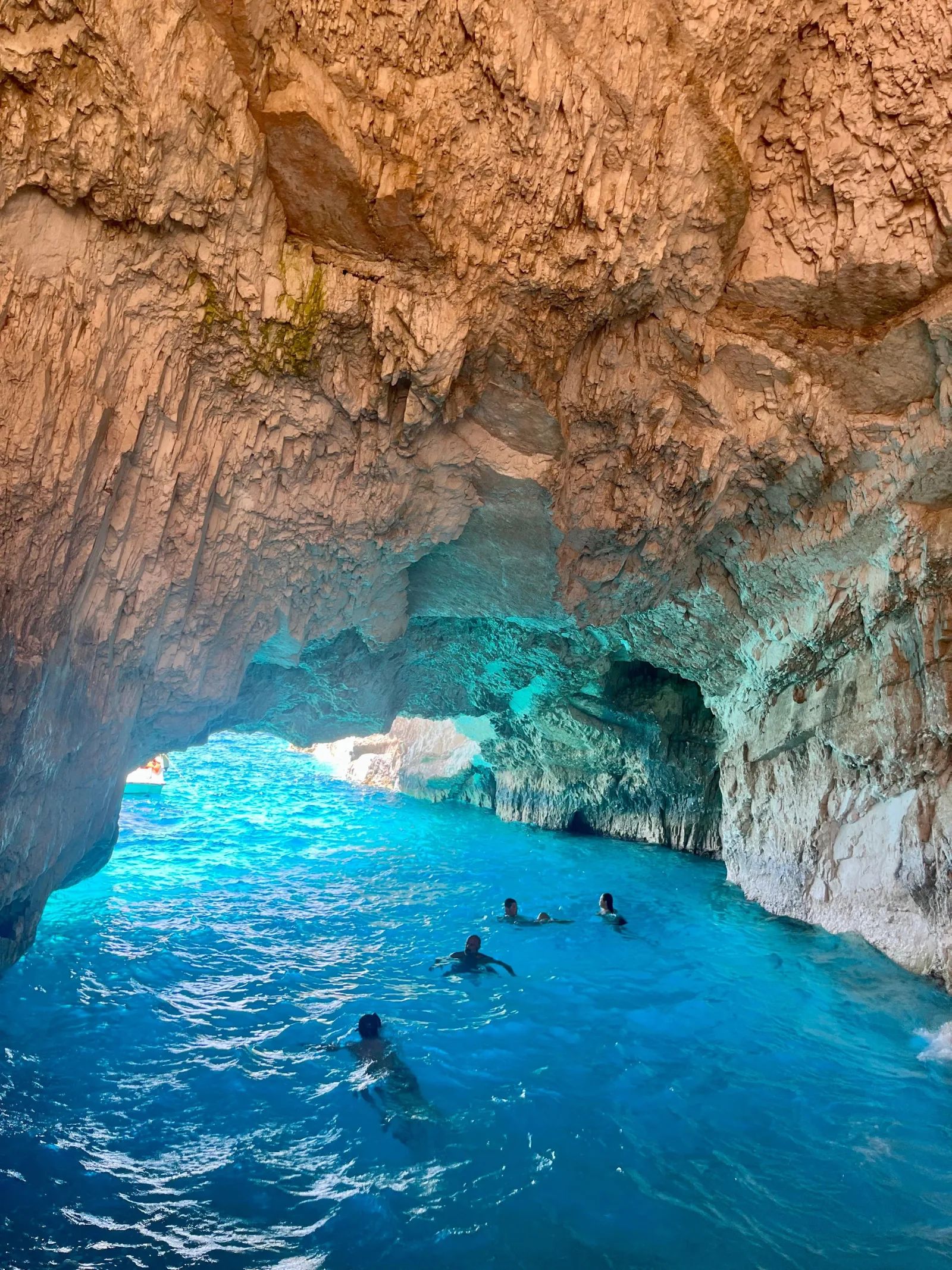 Swimmers in electric-blue water inside a Blue Caves arch beneath ochre limestone
