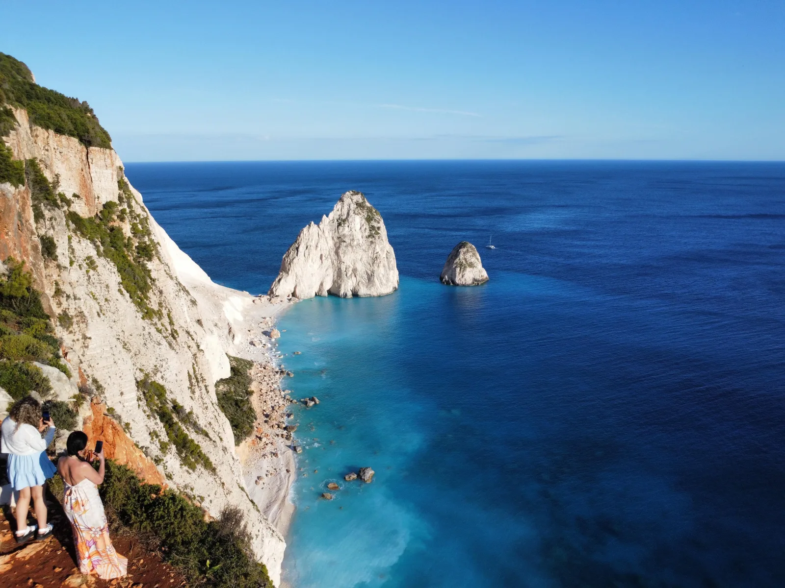 Guests on the cliff edge looking down on the Mizithres rocks and the deep blue sea