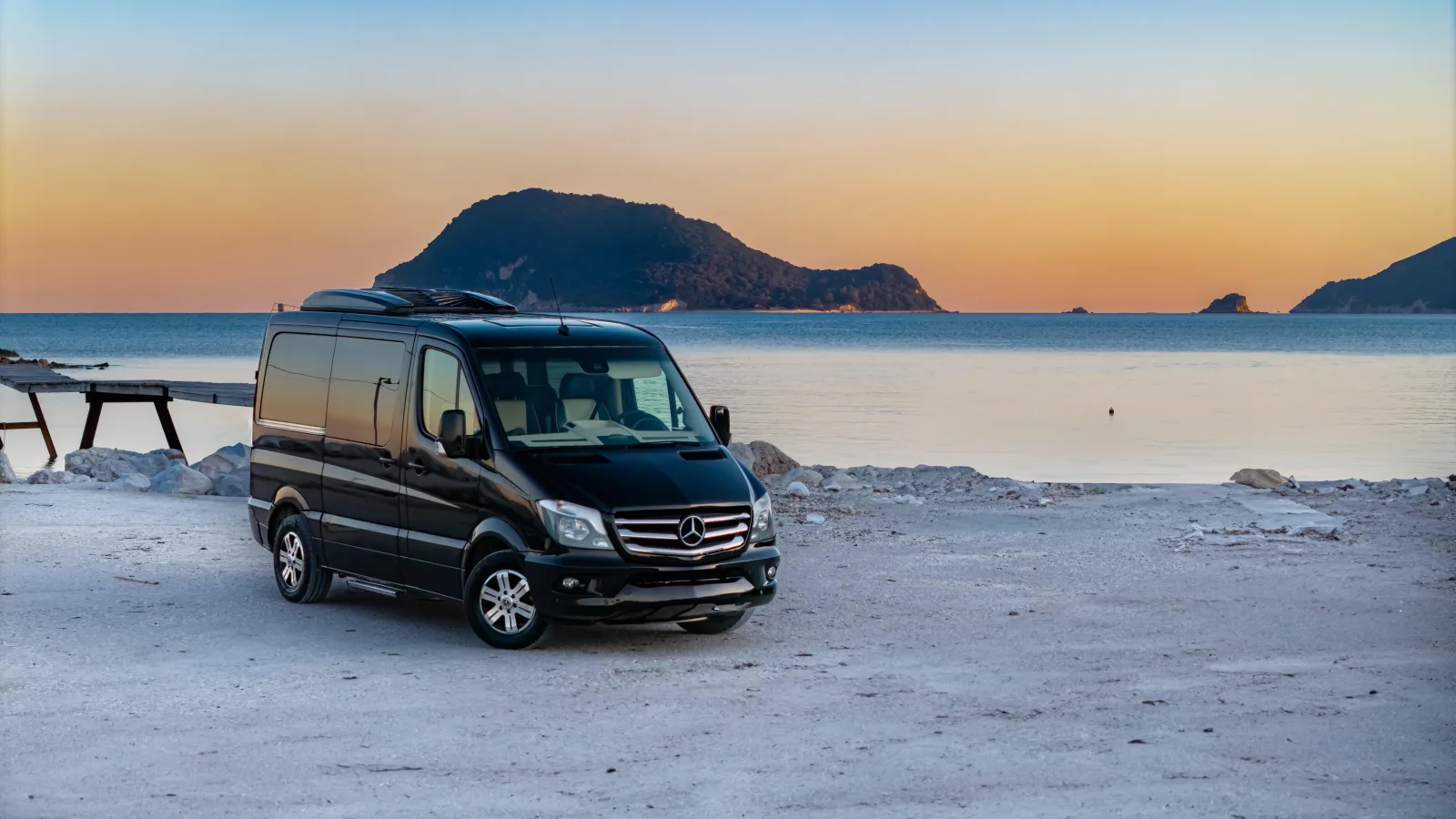 The tour's black minibus parked beside the sea at sunset