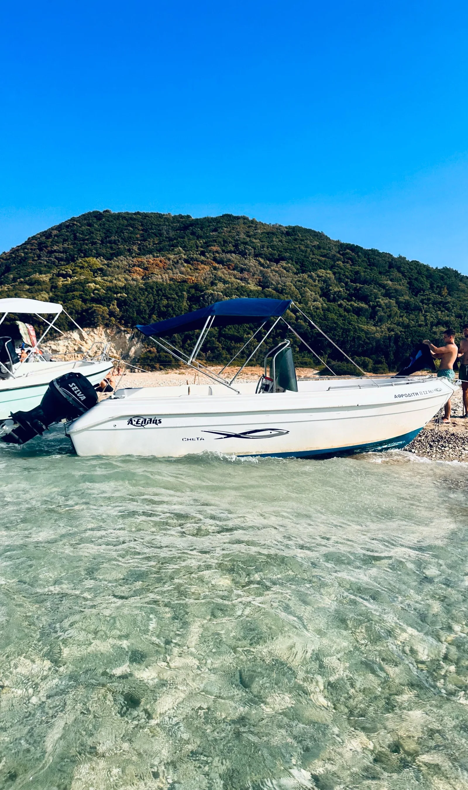 A speedboat with a sun canopy in shallow clear water beside the shore