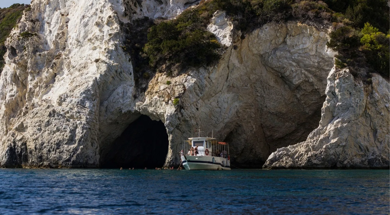 A wooden taxi boat inside a sea cave beneath a pale limestone arch on the south coast
