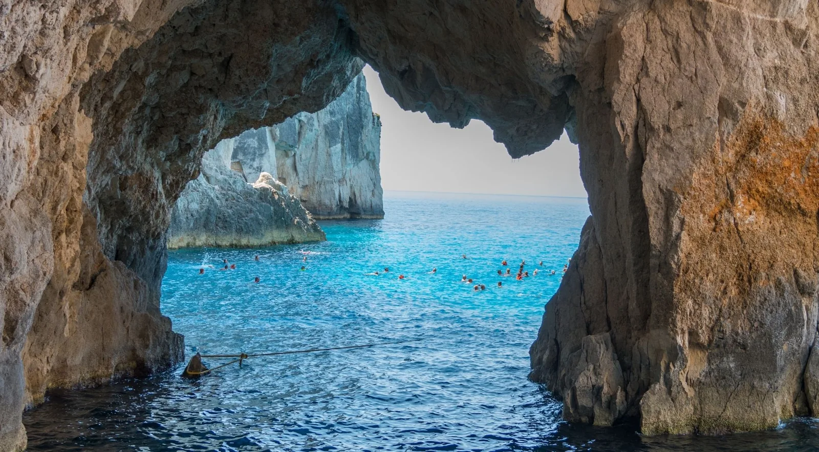 Swimmers inside a Keri sea cave looking out through a wide arch to open water